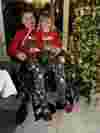 Boy on a wheelchair with his sister on his lap, both wearing christmas jumpers, , smiling whilst next to a christmas tree