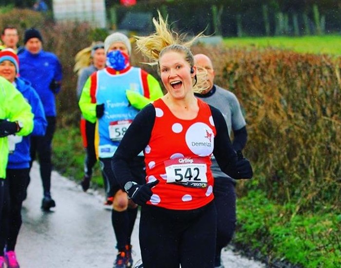 A runner is smiling, wearing her Demelza polka dot running vest.