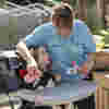A woman in a light blue shirt blowing into a bubble wand with a young girl sitting in an arm chair
