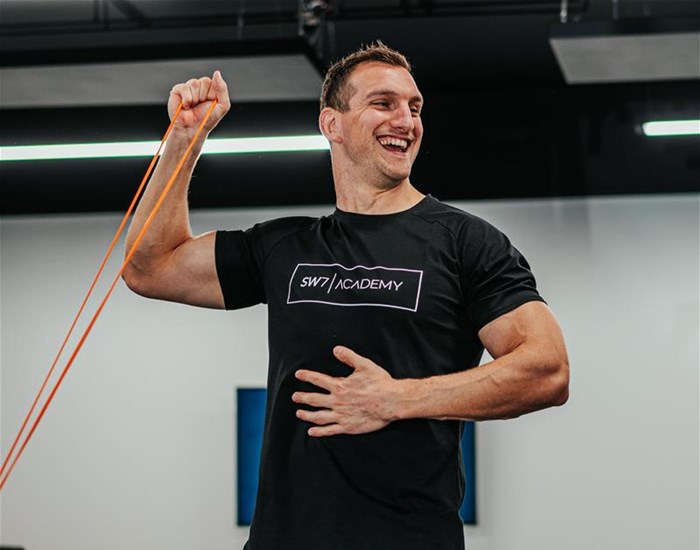 A man in a black t-shirt exercising his arms with a resistance band.