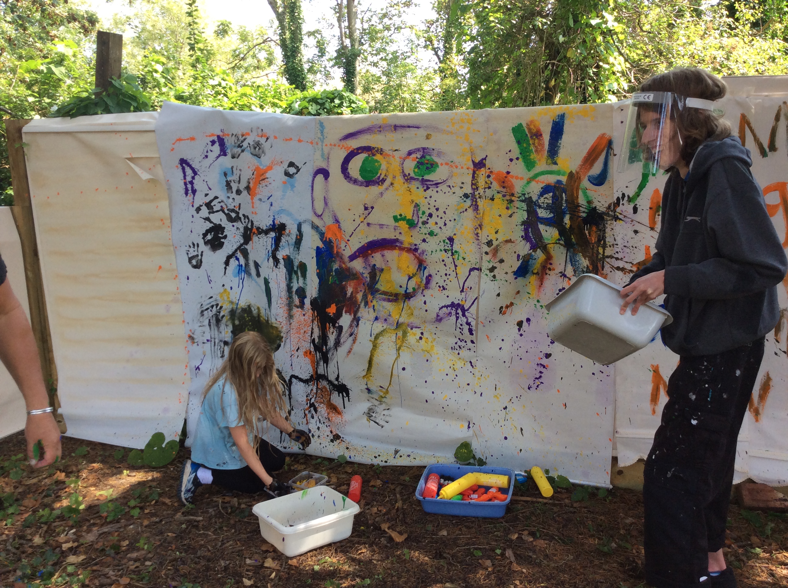 A young person and a child enjoy a painting activity in the garden at Demelza East Sussex site.