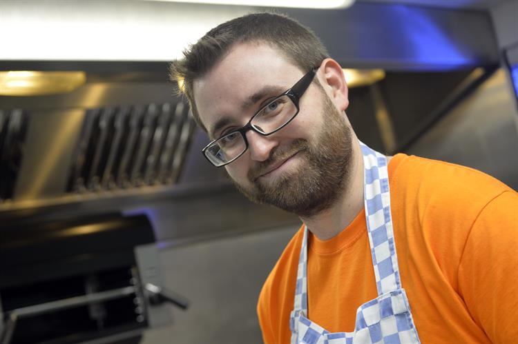 Demelza Chef, wearing an orange t-shirt and blue and white cheque apron.