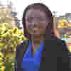 Trustee Dr Jenneh Tarawally stands in sunny gardens, wearing a smart blue dress and black blazer jacket