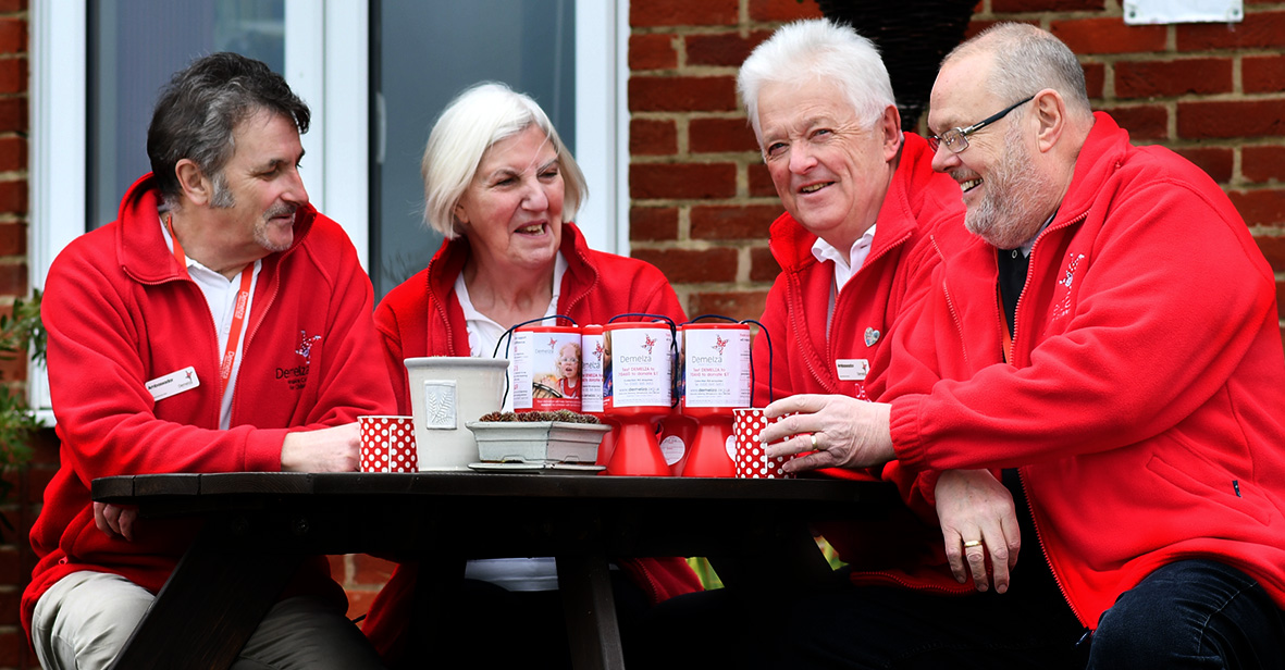 A group of practical support volunteers sit together around a table, with collection pots.