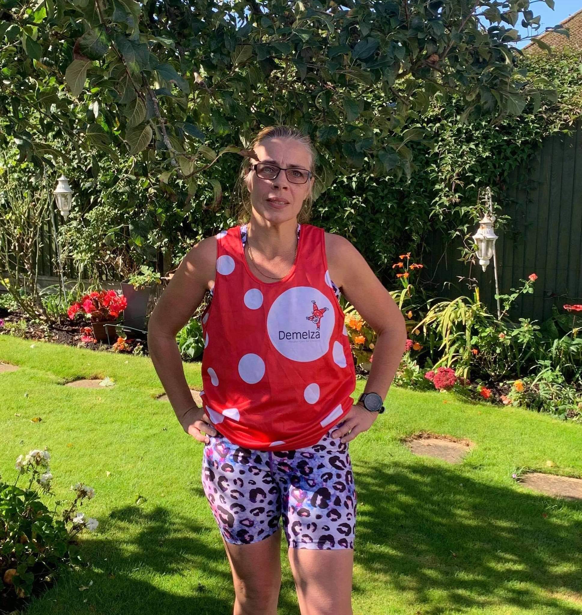 A woman, in her garden, wearing a Demelza running vest and her leopard print shorts.