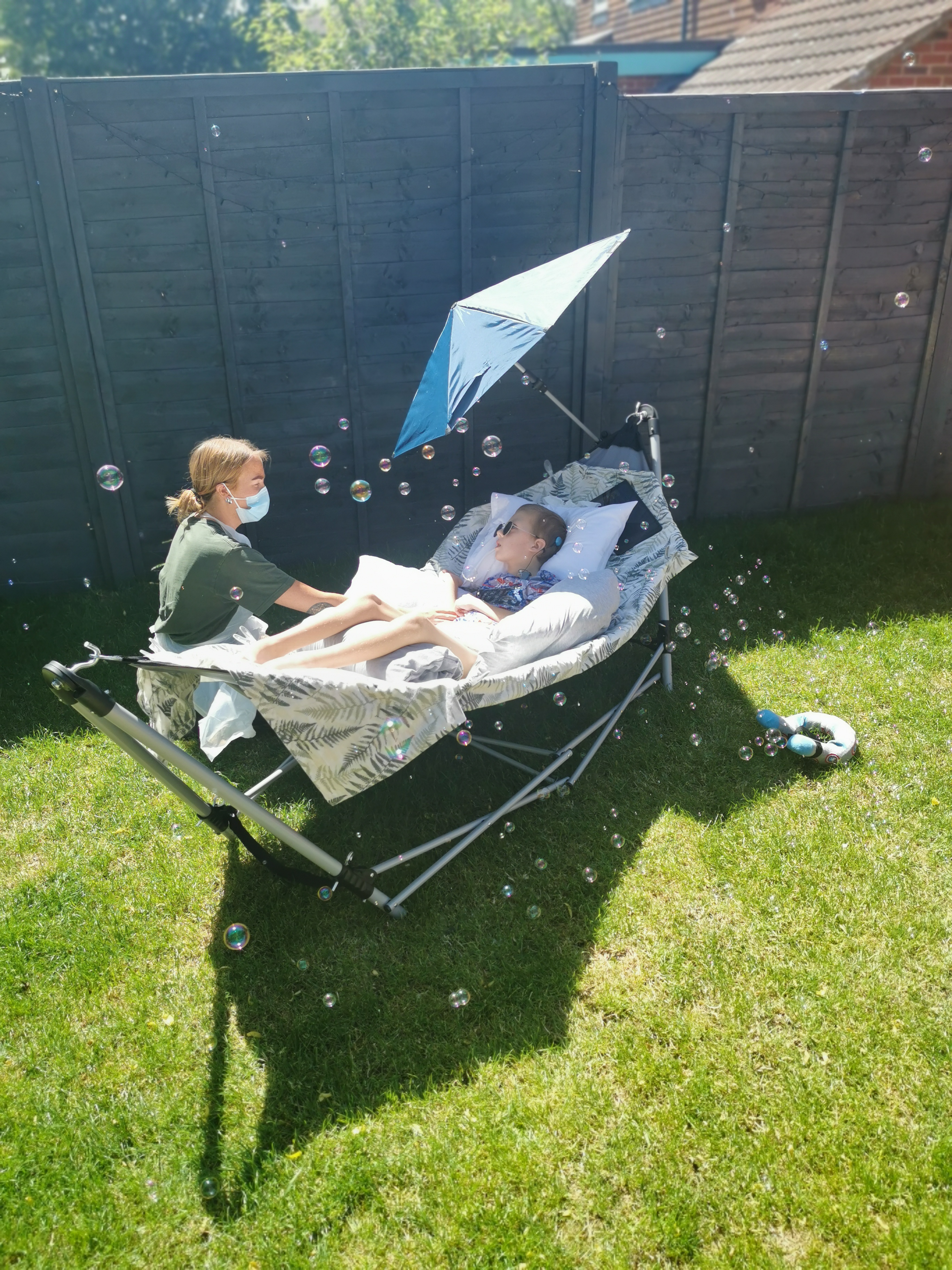 A health care assistant administering care to a young boy, who is enjoying the sunshine in his garden.