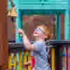 A young boy with glasses ringing a bell in the playground at Demelza Kent