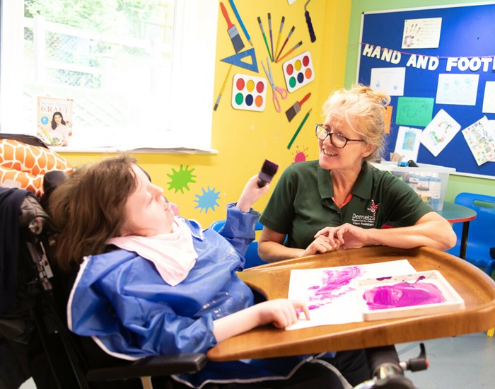 Bethany enjoys a art activity with a Demelza health care assistant helping, crouched down beside her.
