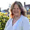 Trustee Susan Tether smiles in sunny gardens, wearing a cream outfit and pearl necklace.