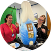 Two women smiling at a camera holding paint brushes in their hand while painting a sculpture of a rabbit