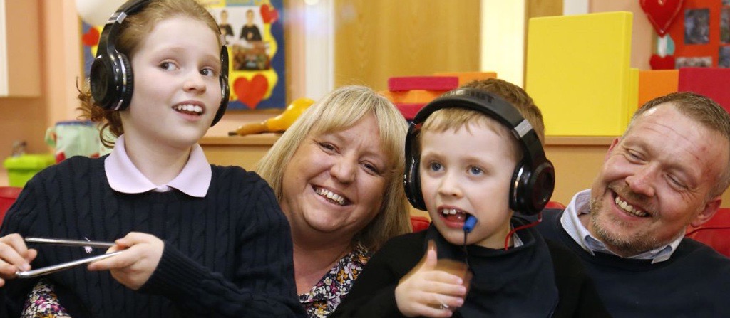 Two children wearing headphones, laughing with their parents.