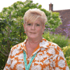 Demelza CEO Lavinia Jarrett stands in the hospice gardens, wearing a bright top and jewellery, smiling warmly.