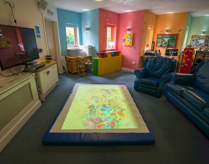 A room with colourful walls, blue sofa's and a light up play mat on the floor.