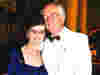Demelza founders Derek and Jennifer Phillips stand side by side at a black tie event, smiling; Jennifer in blue, Derek in white jacket.