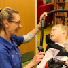 A nurse with glasses smiling towards a child in a wheelchair