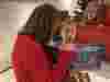 Person in red sweater kneels and reads 'WHY, OH WHY, AM I A CROCODILE?' to two children on a red chair.