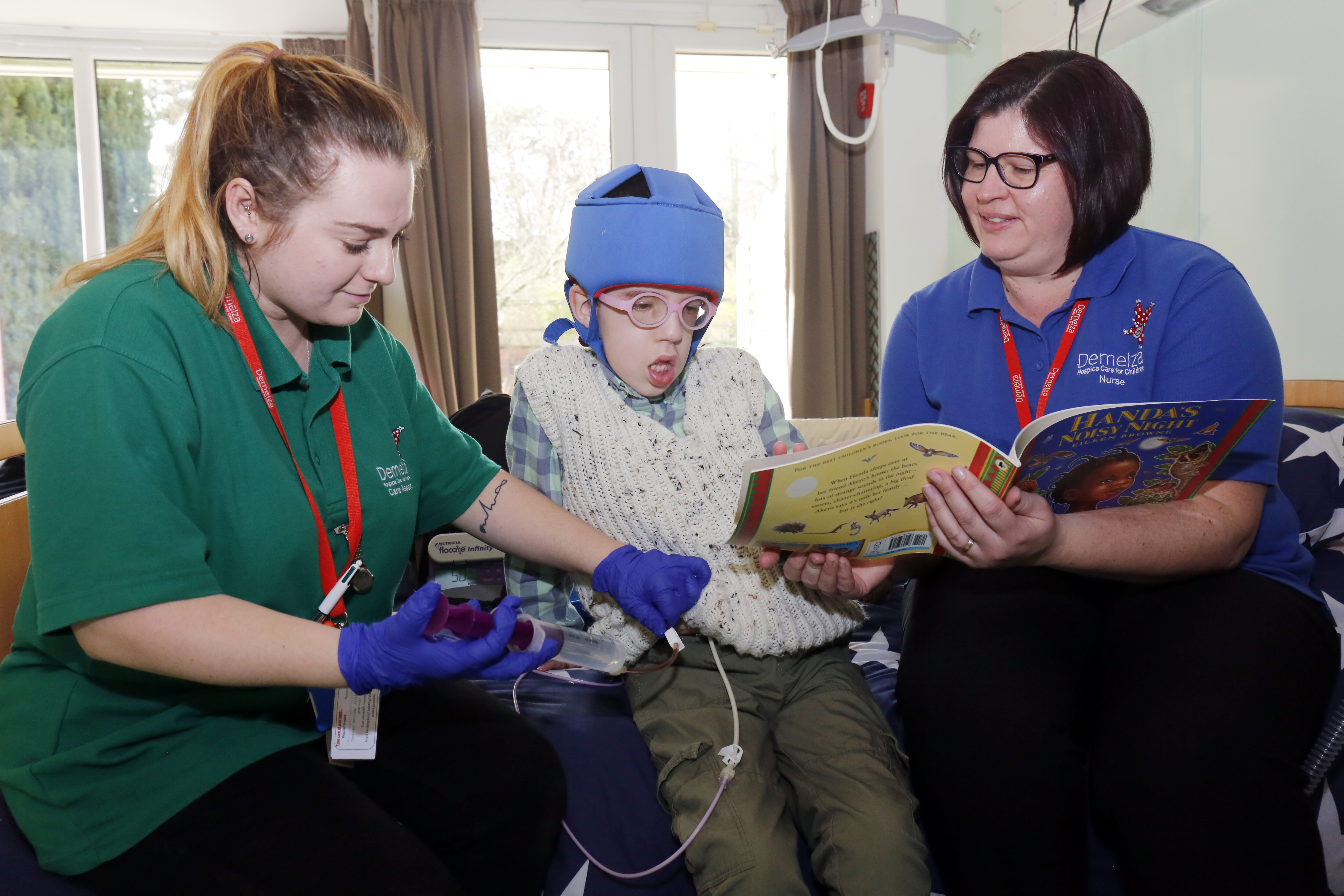 Jack sits on his bed, reading with a nurse, whilst another nurse is administering medication.