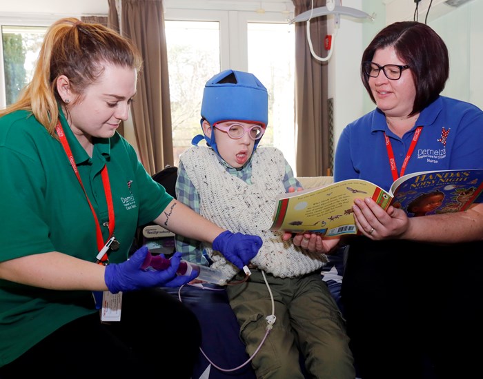 Jack sits on his bed, reading with a nurse, whilst another nurse is administering medication.