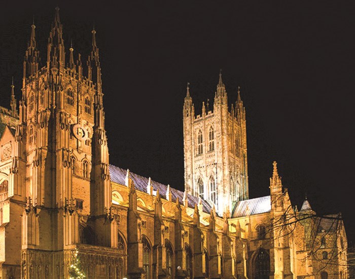 Canterbury Cathedral is light up with lights against a dark night sky.