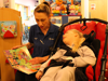 A nurse reading a storybook to a young girl in a wheelchair at Demelza SEL