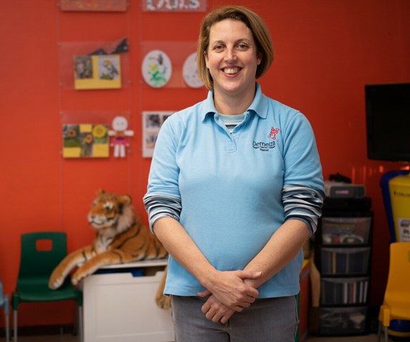 Jenna is wearing a blue polo top and is standing in the play room at East Sussex.