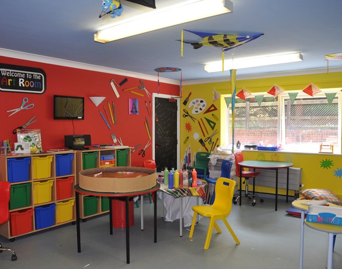 The art room has red and yellow walls and is filled with art equipment.
