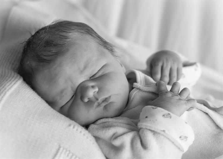 A baby, fast asleep with their hands resting on their chest.