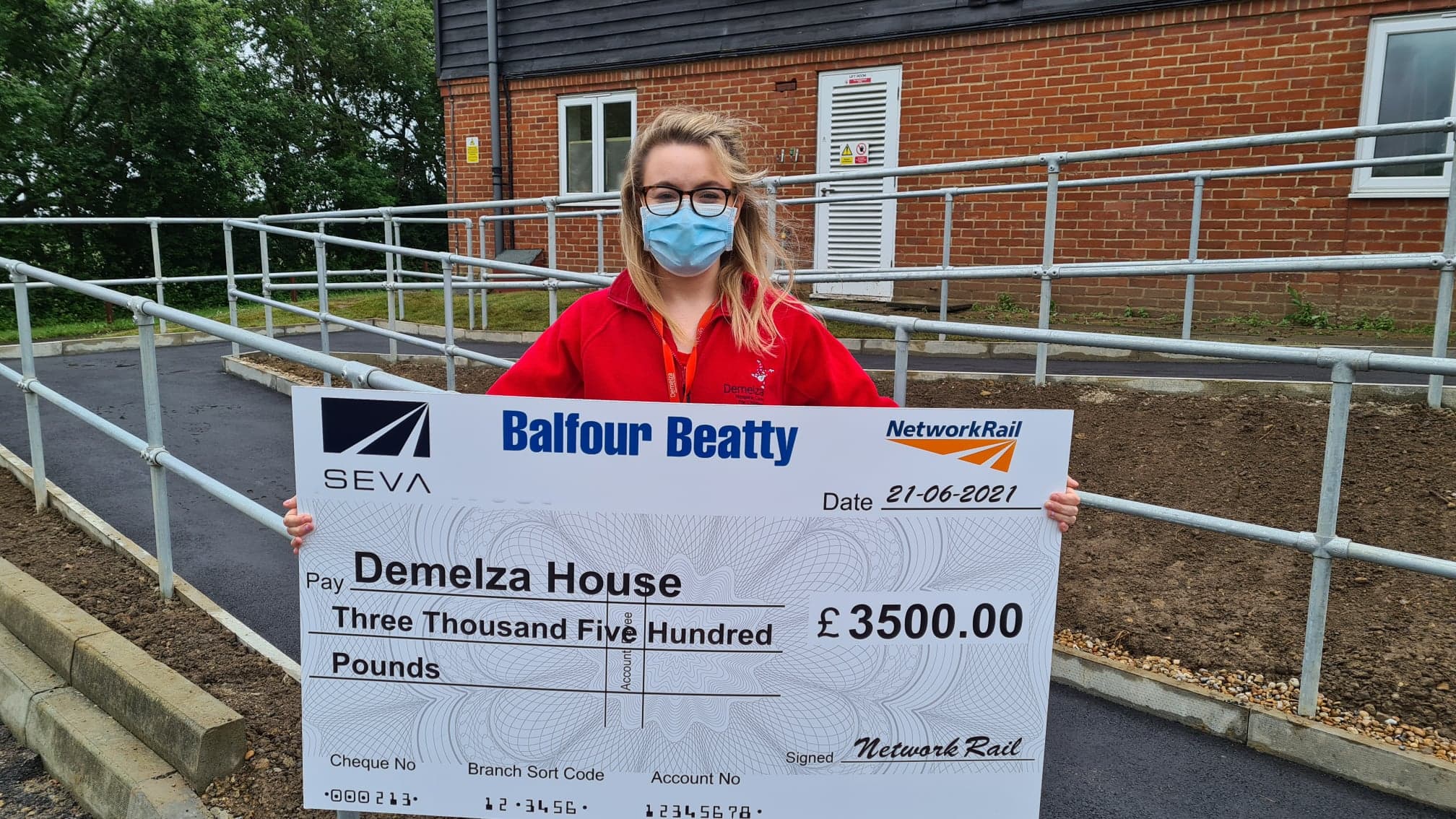 Mary holds a large cheque in front of Demelza new ramp.