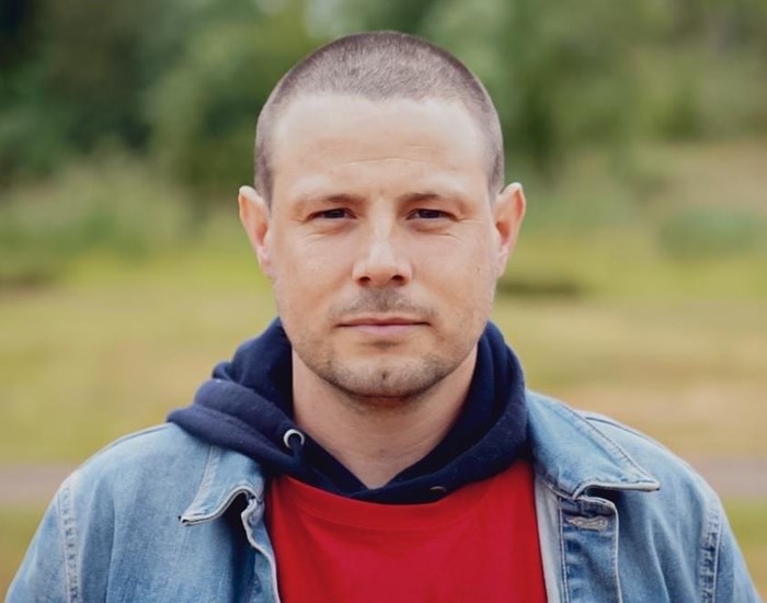 A man wearing a red Demelza t-shirt and denim jacket.