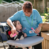 A woman in a light blue shirt blowing into a bubble wand with a young girl sitting in an arm chair