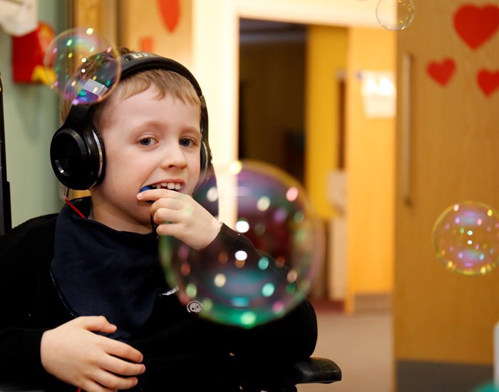 A boy wearing headphones looks at bubbles floating in front of him.