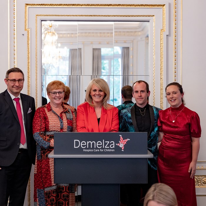 Five smartly dress people, stand being a Demelza branded lectern at the autumn lunch.