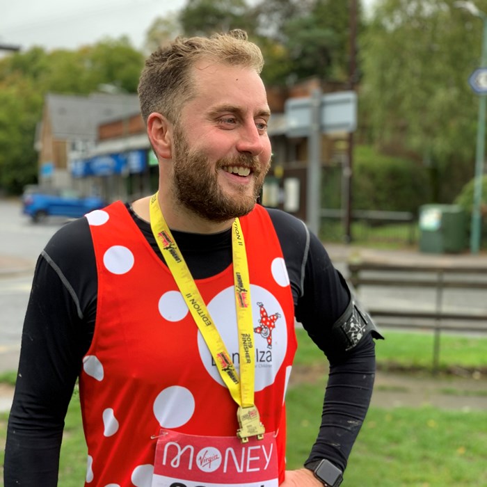 Gavin is wearing his Demelza dotty running vest over a black long sleeve top, wearing a medal.