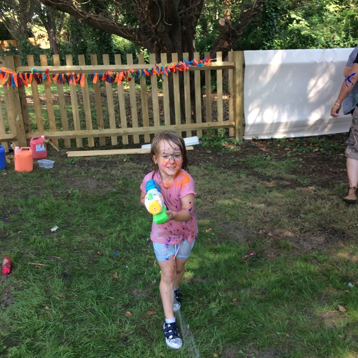 A girl with paint on her face, aims her water pistol at the camera.