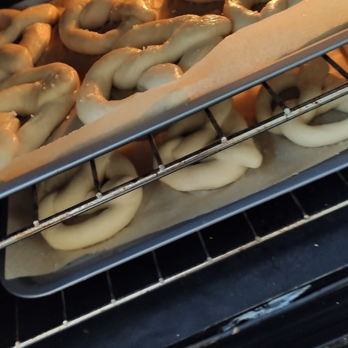 Two trays of large pretzels baking in an oven.