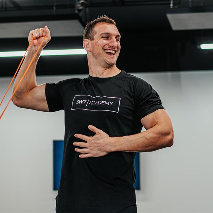 A man in a black t-shirt exercising his arms with a resistance band.