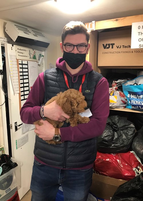  Tanguy is standing in the stock room holding a small puppy.