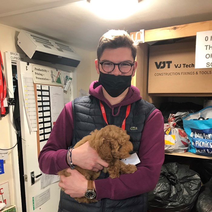  Tanguy is standing in the stock room holding a small puppy.