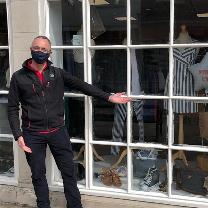 Former CEO Ryan Campbell standing outside a Demelza charity shop window, wearing a black face mask.