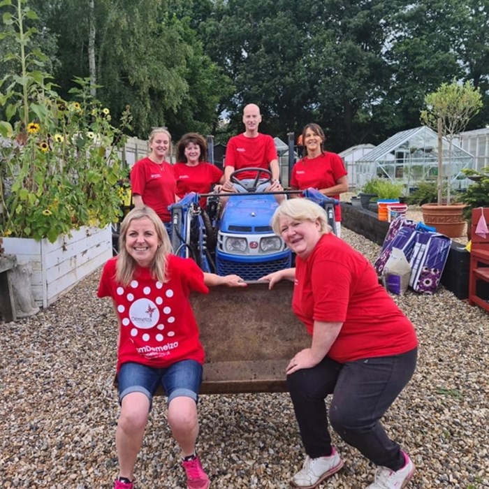 Volunteers wearing Demelza tops, pose together around a small tractor in the hospice gardens.